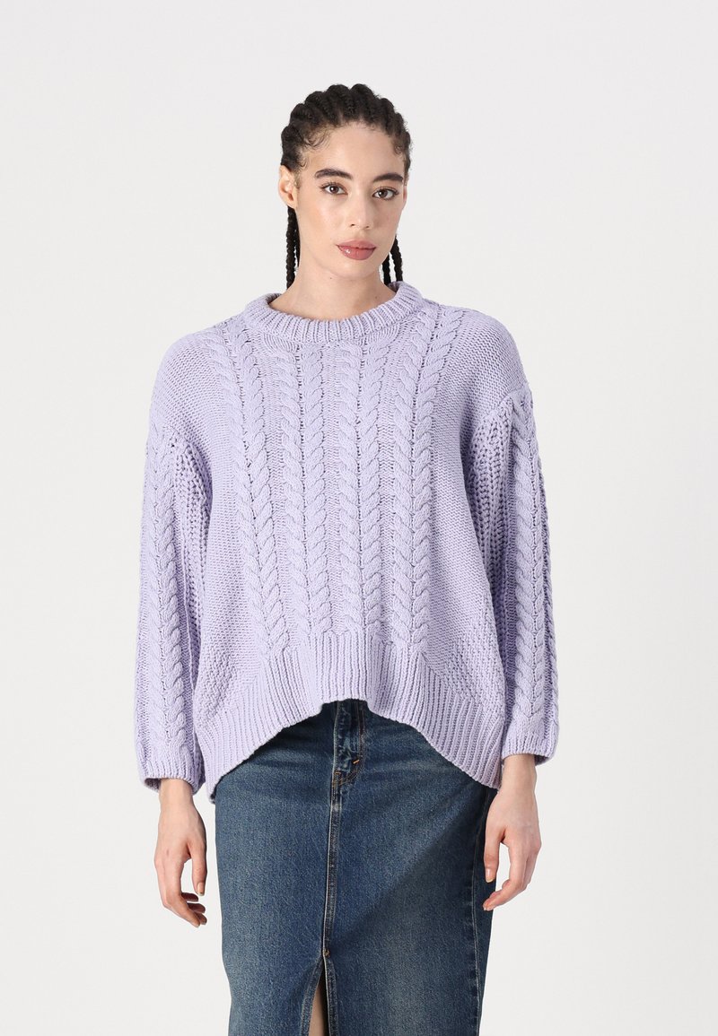 Pull en maille lavande avec un motif de torsades épaisses, ourlet côtelé et manches larges, associé à une jupe en denim avec une fente à l'avant.