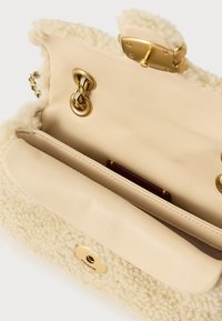 Ramična torba iz kremastega ovčjega usnja in usnja, odprta, da pokaže notranjost, z zlato verižico in zlatim zapiranjem na zaponko.