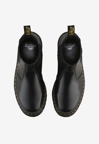 Bottes Dr. Martens en cuir noir à enfiler avec couture jaune et boucles de talon brandées, vues de dessus sur un fond blanc.