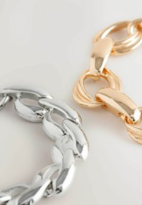 Metal chain links, one silver and one gold, feature a smooth, shiny surface. The gold link has a twisted accent design; the silver is simple.