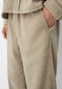 Conjunto de pana beige con textura de canales verticales, corte relajado, bolsillos laterales y detalles de botones en los puños de la chaqueta y en los pantalones.