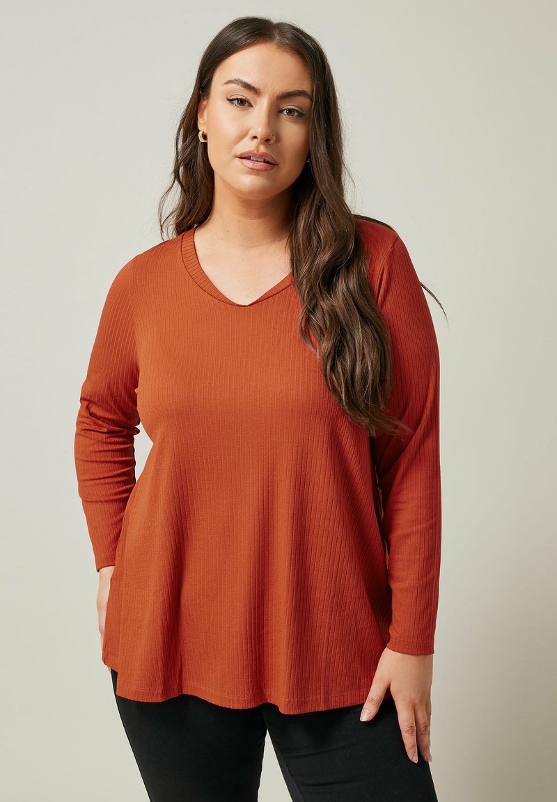 Ribbet, langærmet top i brændt orange med V-halsudskæring. Stoffet er blødt, let struktureret og har en afslappet, blød pasform.