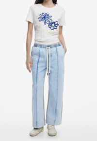 T-shirt en coton blanc avec broderie florale bleue et crème, associée à un pantalon bleu clair à coupe décontractée, bandes latérales et taille à cordon.