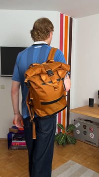 Orange waterproof backpack with a roll-top design, adjustable straps, a front pocket, and black accents. Textured finish.