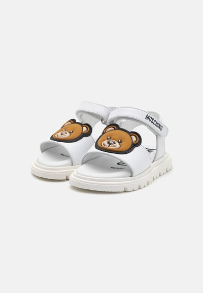 Sandali bianchi con un design a faccia d'orso sulla fascia, realizzati in materiale sintetico, dotati di fasce regolabili e di una suola testurizzata.