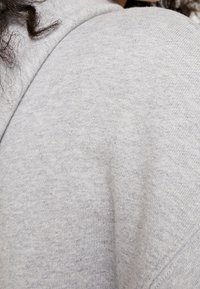 Lockigt mörkt hår som vilar på ett grått stickat tyg, med en närbild av axeln och en del av nacken.