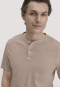Helles beiges Kurzarm-Henley-Shirt mit rundem Halsausschnitt, zwei Knöpfen und einer weichen, glatten Textur.