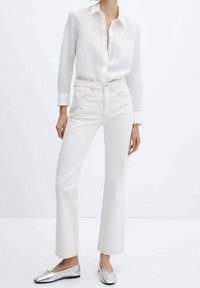 Chemise en lin blanche avec un col, associée à un jean droit beige clair et des chaussures plates argentées. Design simple et textures lisses.