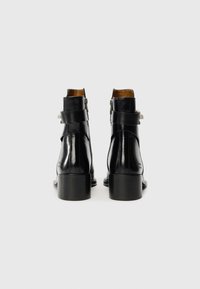 Bottines en cuir noir avec une finition texturée, dotées d'une fermeture éclair sur le côté, de détails de sangle et d'un solide talon carré.