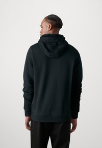 Hanorac negru cu glugă spațioasă, mâneci lungi și manșete cu dungă. Materialul pare neted cu un finisaj mat. Design simplu, fără modele.