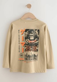 Barna hosszúujjú póló, amelyen egy grafikai nyomtatás látható egy fejhallgatós gorillával és egy kontrollerrel, narancssárga és fekete szöveggel kiemelve.