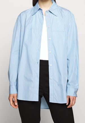 Ljusblå randig skjorta med knappar som är gjord av bomull. Har en klassisk krage, två framfickor och långa ärmar med knäppning vid manschetterna.