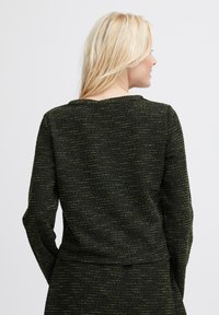 Czarny sweter o fakturze z zielonymi drobinkami, długie rękawy i okrągły dekolt. Materiał ma tkany wzór i subtelną poświatę.