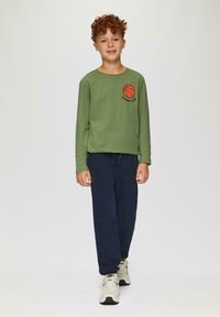 Lange mouwen groen shirt met een basketbalafbeelding en de tekst "DUNKIN' CLUB", gecombineerd met marineblauwe trainingsbroek en neutrale sneakers.