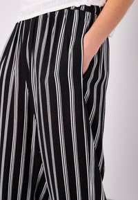 Black and white striped wide-leg pants featuring a comfortable elastic waistband and side pockets, made from lightweight fabric.