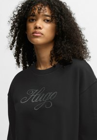 Felpa nera con vestibilità rilassata, scollo rotondo e decorazione in strass argentati con la parola "Hugo" in un carattere corsivo.