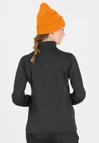 Svart långärmad tröja med hög krage och textilstruktur. Kombineras med en ljusorange stickad mössa. Diskreta detaljer på ärmarna.