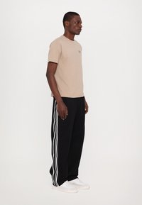 Beige bavlněné tričko s krátkým rukávem, v kombinaci s černými sportovními kalhoty s bílými pruhy a bílými teniskami.