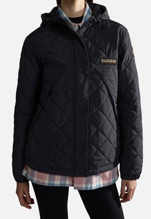 Persona vistiendo una chaqueta acolchada negra con capucha sobre una camisa de cuadros en tonos pastel y pantalones negros, mostrada desde el cuello hasta las caderas.