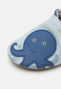 Scarpa di pelle azzurro chiaro con design di polpo blu. Presenta dettagli cuciti, occhi rotondi e motivi ondulati lungo il lato.