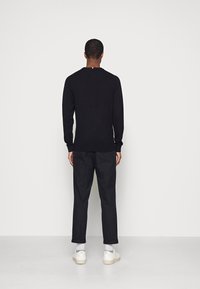 Schwarzer langärmliger Pullover mit Rundhalsausschnitt, glatter Textur und enganliegenden Bündchen, kombiniert mit maßgeschneiderten schwarzen Hosen und weißen Turnschuhen.