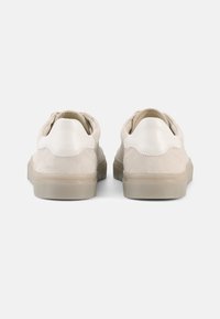 Μπεζ σουέντ αθλητικά παπούτσια με λείο λευκό δερμάτινο πίσω μέρος, στρογγυλεμένο σχήμα και διαφανές ελαστικό πέλμα. Μινιμαλιστικός σχεδιασμός χωρίς σχέδια.