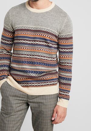 Pull en tricot multicolore avec des motifs géométriques en bleu, orange et bordeaux, featuring un col rond beige et des bords côtelés aux poignets et à l'ourlet.