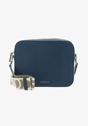 Sac bandoulière rectangulaire en cuir bleu marine avec une sangle en tissu beige et blanche ajustable et un logo "Coccinelle" doré sur le devant.