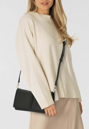 Bolso bandolera de cuero negro con acabado texturizado, forma rectangular, correa ajustable, sostenido contra un suéter de punto beige claro.