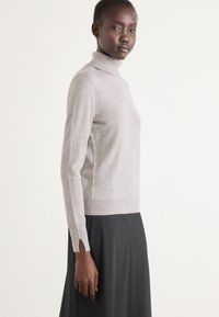 Lys grå turtleneck sweater med lange ærmer, med sideslids ved ærmekanterne. Blød tekstur, tætsiddende design og minimale sømme.