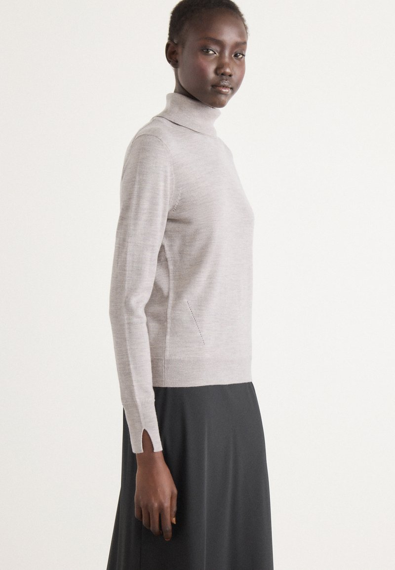 Lys grå turtleneck sweater med lange ærmer, med sideslids ved ærmekanterne. Blød tekstur, tætsiddende design og minimale sømme.