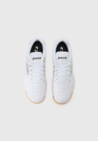 White athletic shoes with a textured leather upper, perforated detailing, and a gum rubber sole. Black inner lining with a logo on the tongue.