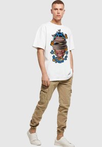 Hvit t-skjorte med fargerik grafisk design av et ansikt og sommerfugler. Kombinert med beige cargobukser og hvite sneakers.