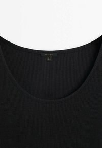 Top sans manches noir côtelé avec un col arrondi et une petite étiquette de marque cousue à l'intérieur du col.