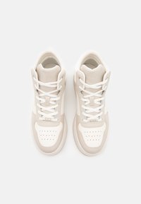 Baskets montantes blanches et beige clair en matériaux en maille et cuir, à bout rond, avec des détails perforés et des lacets plats. Design simple et moderne.