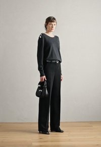 Pull en maille noir avec détail de boutons à l'épaule, associé à un pantalon noir taille haute, une ceinture noire et un petit sac à main noir.