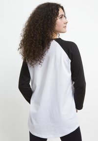 T-shirt raglan bianco e nero con maniche lunghe nere e orlo curvo, realizzato in tessuto morbido, con una vestibilità comoda e un design semplice.