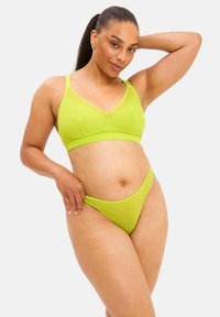 Lys limegrønt lingerisæt bestående af en bralette med meshnets og matchende højskårne trusser, begge lavet af glat, strækbart stof.