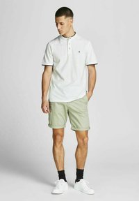 Witte polo met zwarte accenten, gecombineerd met lichtgroene shorts. Beschikt over een twee-knopen placket, opgerolde mouwen en witte sneakers.