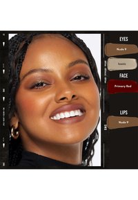 Donna sorridente con capelli intrecciati, che indossa orecchini a cerchio dorati, ombretto caldo, blush rosso e rossetto nude su pelle marrone chiaro.