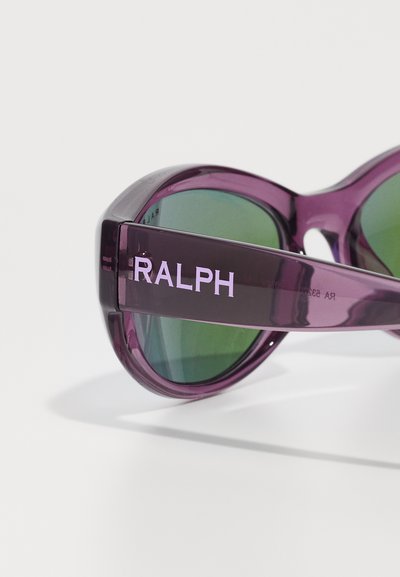 Occhiali da sole viola con lenti verdi. La montatura è realizzata in un materiale lucido e presenta il nome "RALPH" in viola chiaro sul lato.