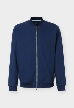 Μπουφάν bomber σε ναυτικό μπλε με μεταλλικό φερμουάρ μπροστά, ριμπ λαιμόκοψη, μανίκια και τελείωμα, καθώς και δύο πλαϊνές τσέπες, παρουσιασμένο σε απλό φόντο.