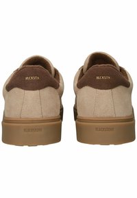 Zapatillas de ante beige con un acento de talón de ante marrón, que presentan un logotipo dorado en relieve "BLCKSTN" y una suela de goma color tostado.