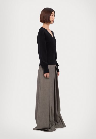 Schwarzer langärmliger Pullover mit V-Ausschnitt, kombiniert mit einem grauen, weit geschnittenen Rock mit Falten und einer glatten Oberfläche.
