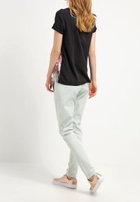 Černé tričko s krátkým rukávem s květinovým motivem, spárované s mintově zelenými tepláky. Obuv má světlý tón s texturou.