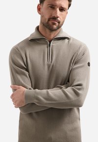 Lichtgrijze geribde trui met een ritskraag, lange mouwen en textiel met structuur, voorzien van een logo-opdruk op de linker schouder.