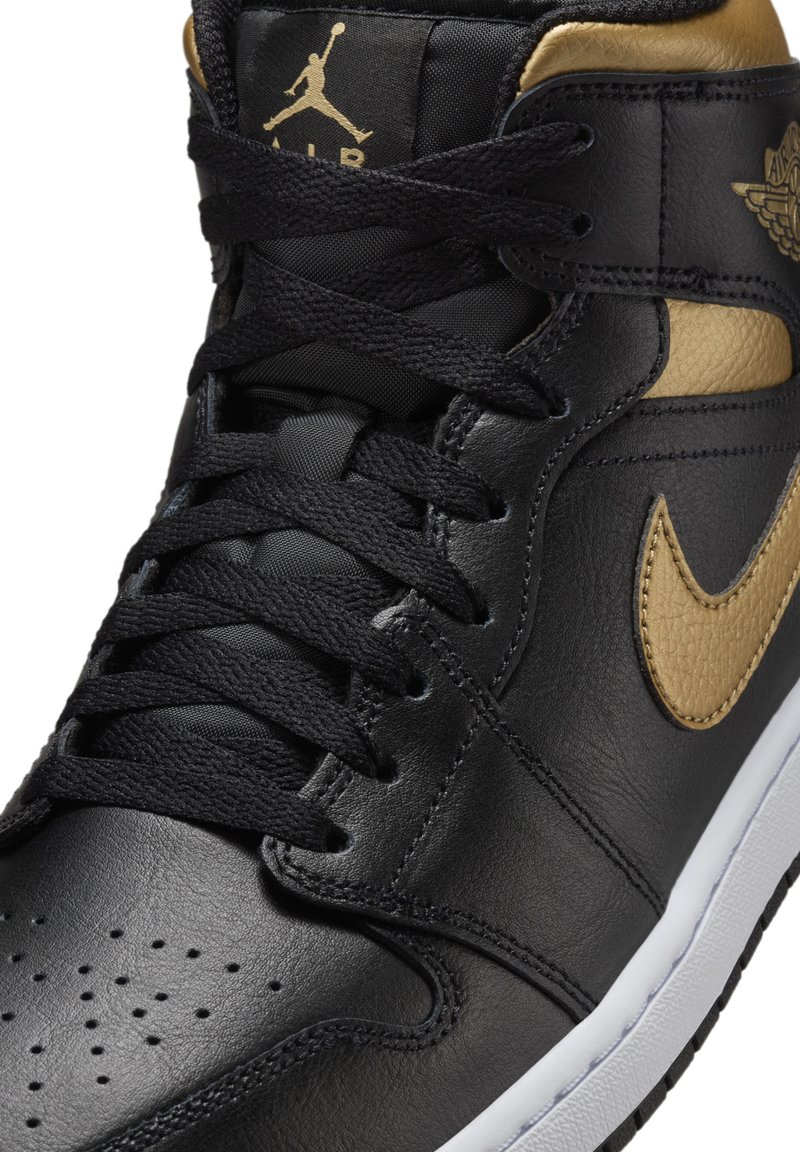 Zwarte leren sneaker met gouden accenten, voorzien van een geperforeerde neus, zwarte veters en een witte zool. Iconisch logo op de tong en zijkant.