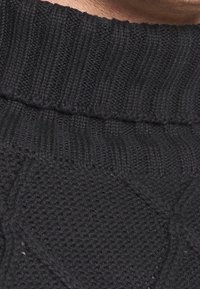 Maglione nero a maglia con un motivo testurizzato, colletto a coste e dettagli di cucitura a contrasto, che enfatizzano calore e maestria artigianale.