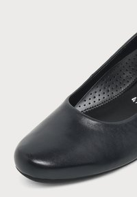 Chaussure plate en cuir noir avec bout arrondi et semelle intérieure matelassée et perforée visible à l'intérieur.