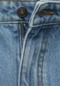 Primo piano di un girovita in denim con un bottone, una cerniera e dettagli di cucitura, che mette in evidenza la texture e il colore del tessuto.